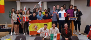 Photo of 23 students posing on a stage with flags from their countries.